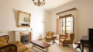 Een kamer met een open haard, een piano en twee gestreepten fauteuils.