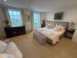 A bedroom with a large bed, a dresser, a bench, a nightstand, and a window with a view.