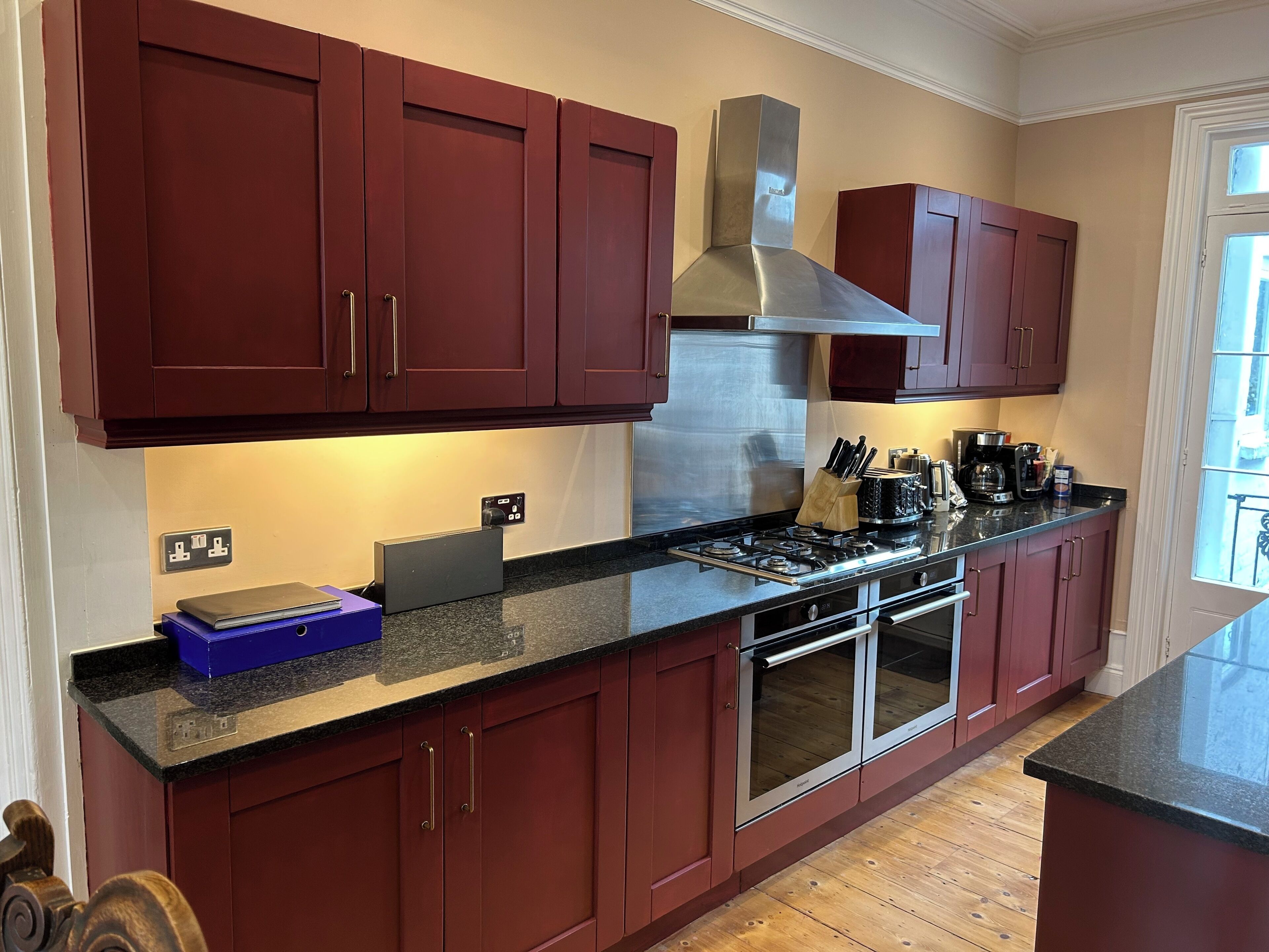 A kitchen with dark red cabinets, a stainless steel range hood, a gas stove, and an oven.