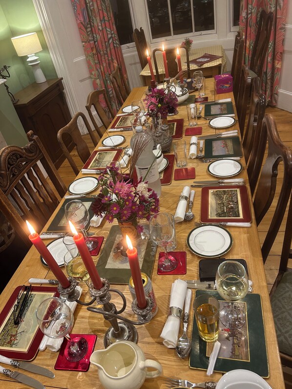 Une longue table à manger, décorée de bougies, d’assiettes, de verres et de couverts, entourée de chaises en bois.