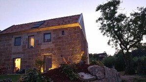 A stone house with a sloped roof, a small garden with plants and a stone wall, and a tree in the background. - A Unique Home, For A Truely Unique Experience (Mos)