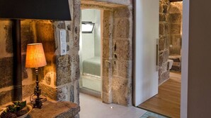 A stone-walled bathroom with a glass shower door, a bedside lamp, and a small plant on a stone ledge. - A Unique Home, For A Truely Unique Experience (Mos)