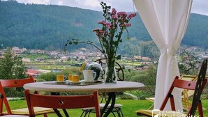 A round table with chairs, a vase with flowers, and a view of a village and hills in the background. - A Unique Home, For A Truely Unique Experience (Mos)