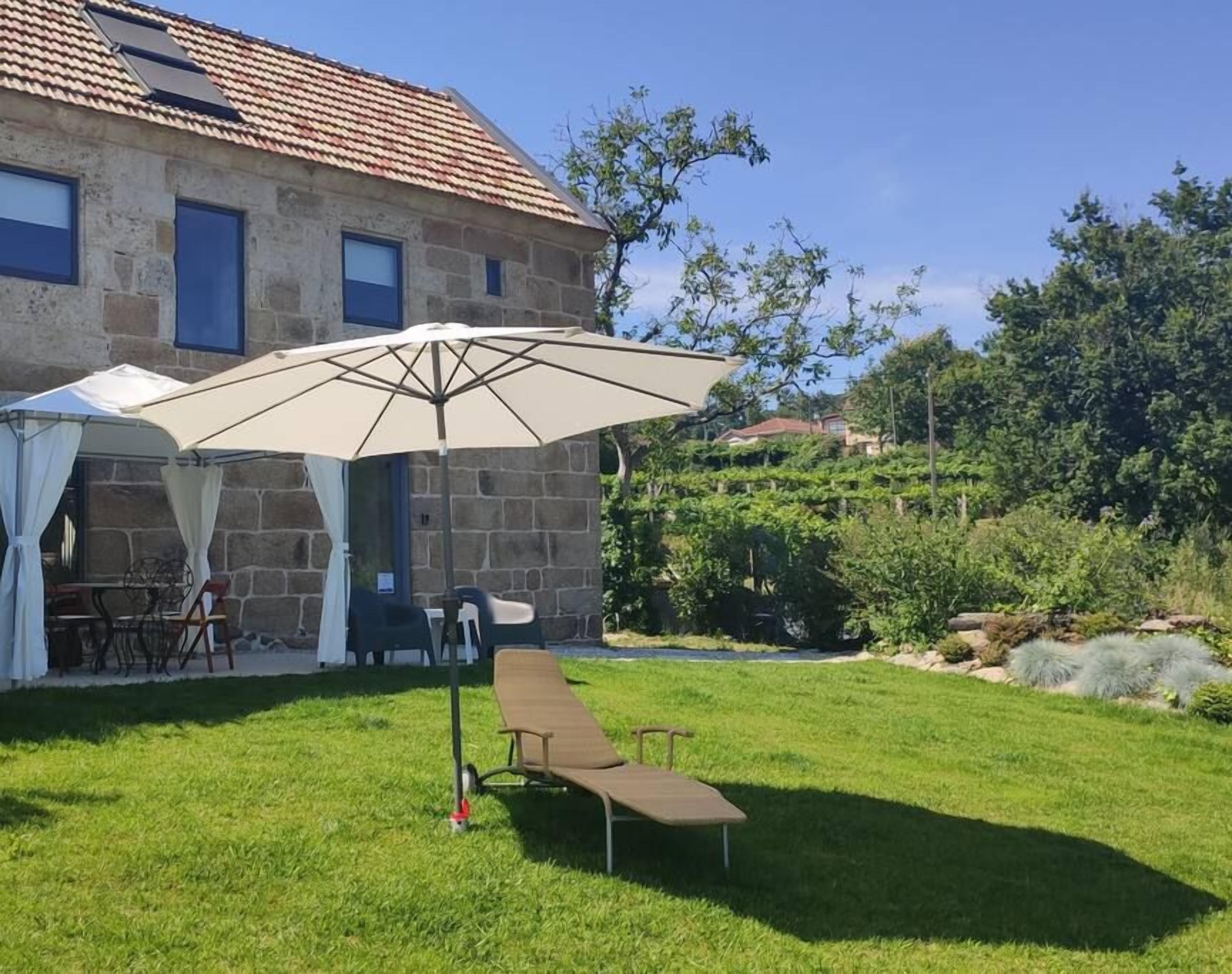 Un bâtiment en pierre avec un toit en tuiles, un espace extérieur abrité avec une table et des chaises, et une pelouse verdoyante avec un banc.