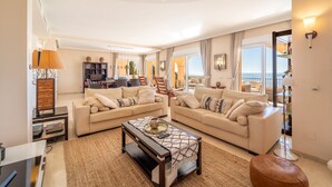 A spacious living room with two sofas, a coffee table, and a bookshelf. There is a balcony with a view of the sea. - Beachside villa with panoramic sea views (Benalm���dena-Costa)
