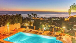 A swimming pool with lounge chairs, surrounded by a landscaped garden and a view of the ocean at sunset. - Beachside villa with panoramic sea views (Benalm���dena-Costa)
