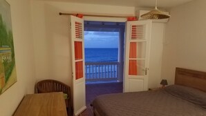 Un dormitorio con cama, escritorio, silla y balcón con vistas al mar.