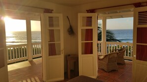 Una habitación con vista al océano, una cama, una silla y una puerta con una escoba apoyada.