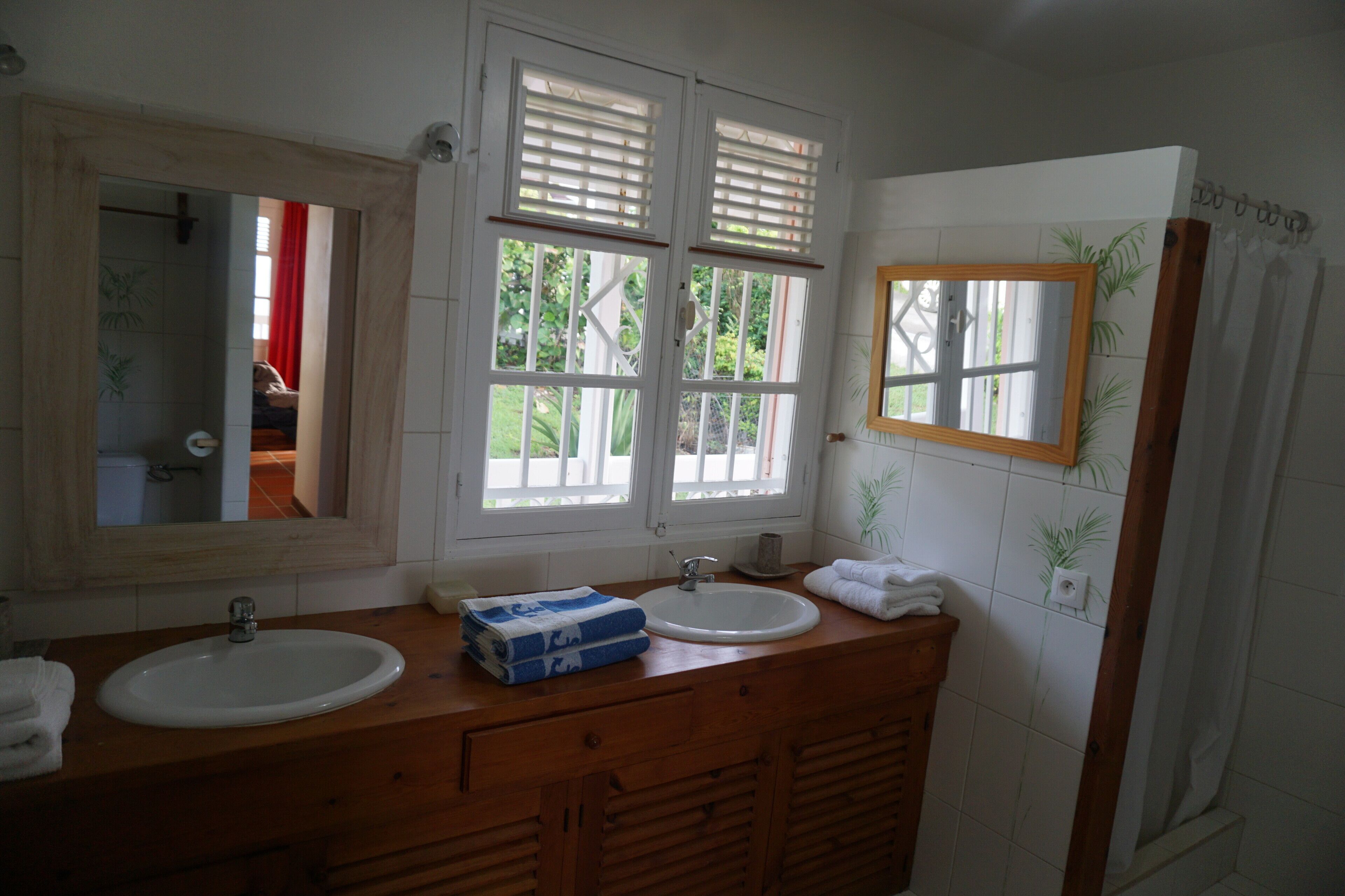 A bathroom with two sinks, a mirror, and a window with shutters.