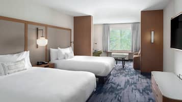 A hotel room with two beds, a desk, a chair, a TV, and a window with a view of trees.