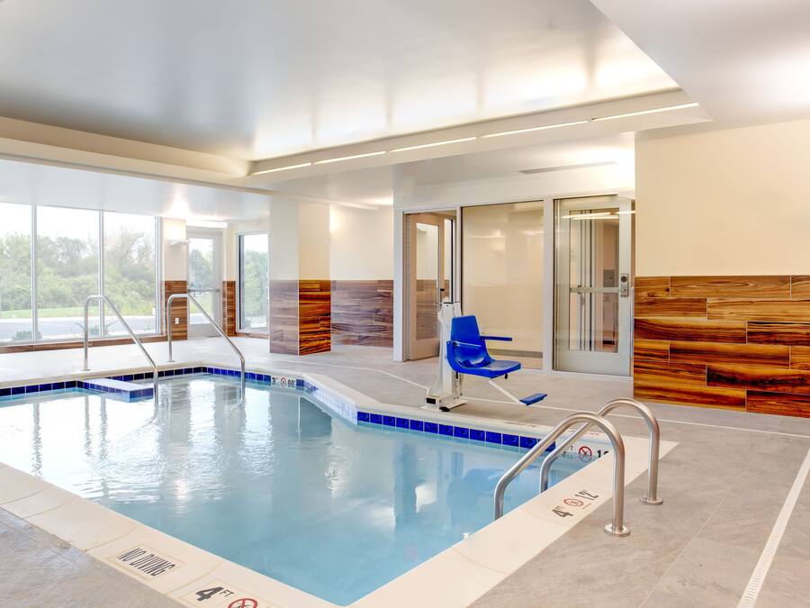 An indoor swimming pool with clear water, a blue chair, and a wooden wall.