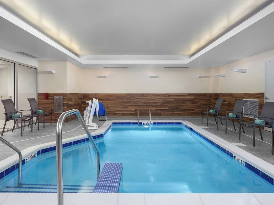 A modern indoor pool area with clear blue water, a wooden wall, and seating with cushions.