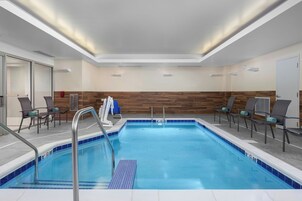 Un área de piscina interior moderna con agua azul cristalina, una pared de madera y asientos con cojines.