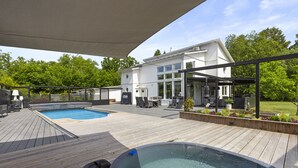 Een moderne buitenzwembadzone met een jacuzzi, houten terras en een overdekte zithoek.