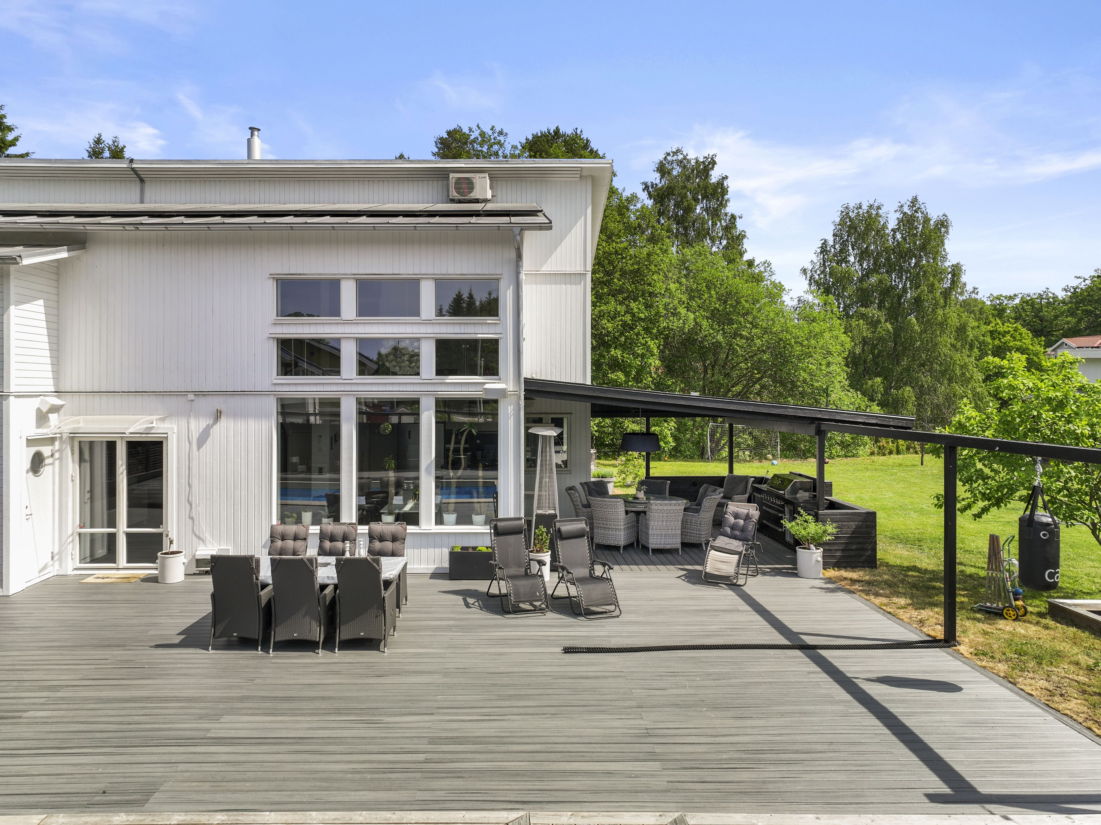Une maison moderne à deux étages dotée d’un patio couvert aménagé avec du mobilier d’extérieur et un barbecue.