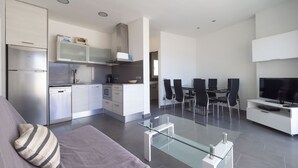 A modern kitchen with stainless steel appliances, a dining area with a glass table and chairs, and a living area with a sofa and a TV. - Amazing apartment on the seafront in Roses Inmosantos Oasis B8 (Rosas / Roses)