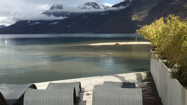 Una terraza junto al lago con sillones de descanso, vista a una cordillera y un lago tranquilo.