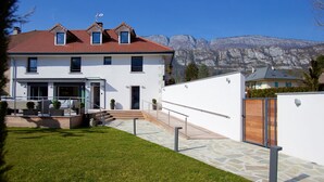Una casa moderna de dos pisos con un camino de piedra que conduce a la entrada, un pequeño jardín y montañas al fondo.