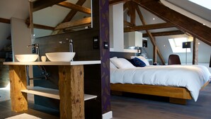 Un dormitorio con una cama de madera, una mesita de noche blanca y un ventanal grande.