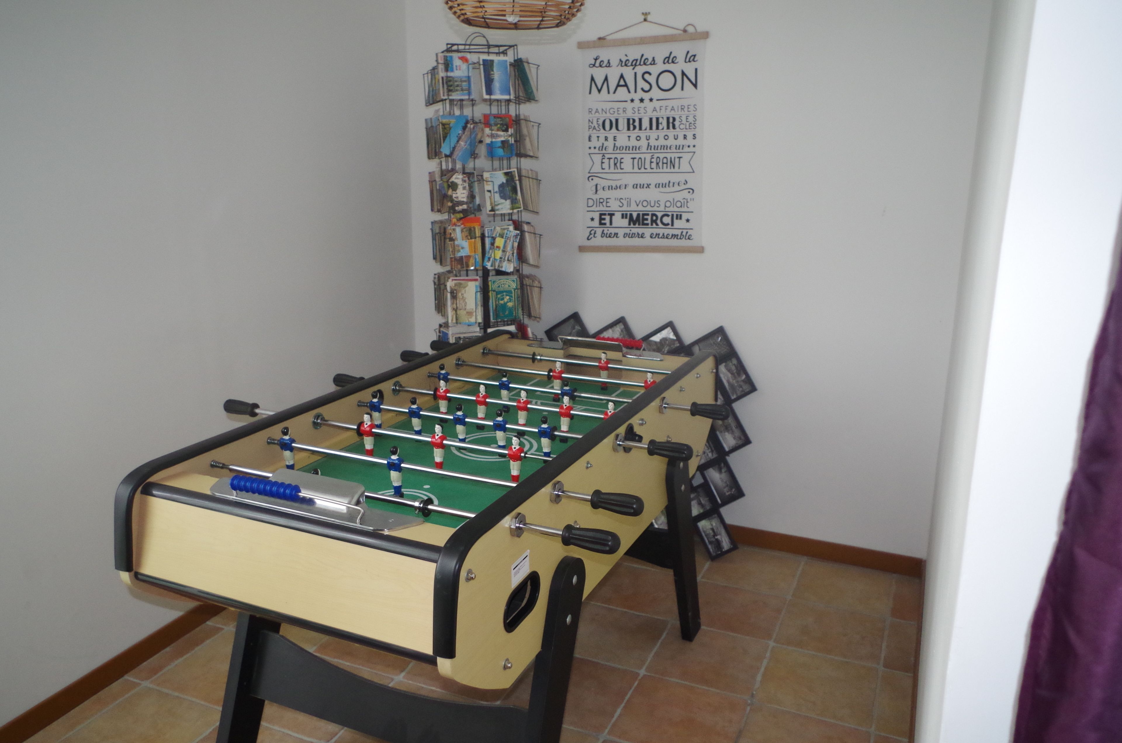 A foosball table in a room with a wall-mounted book rack and a poster with French text.