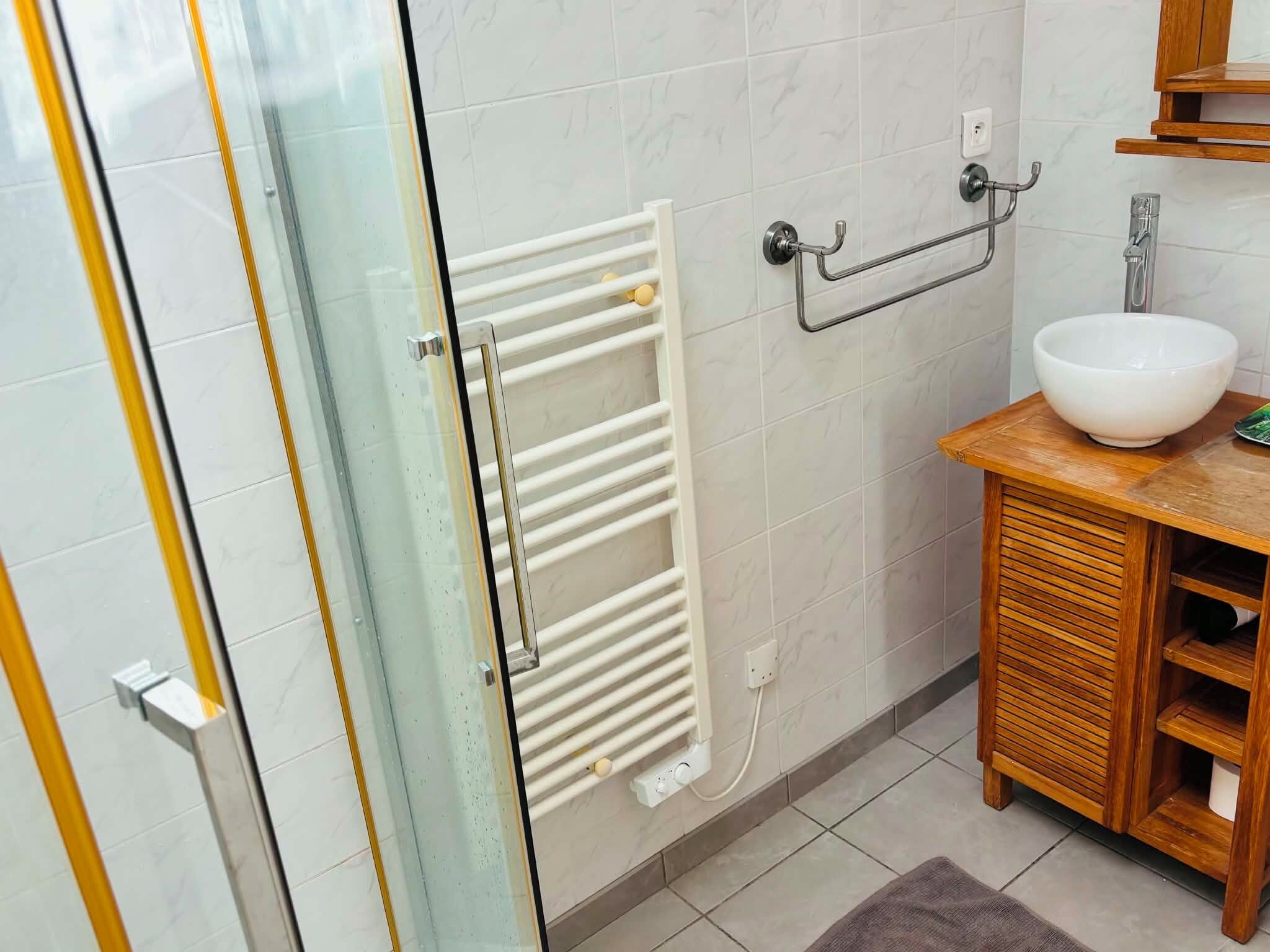 Une salle de bain avec une porte de douche en verre, un porte-serviettes blanc, un meuble en bois avec un lavabo et un bac blanc.