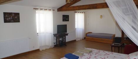 A bedroom with a bed, a television, a desk, and a window with curtains.