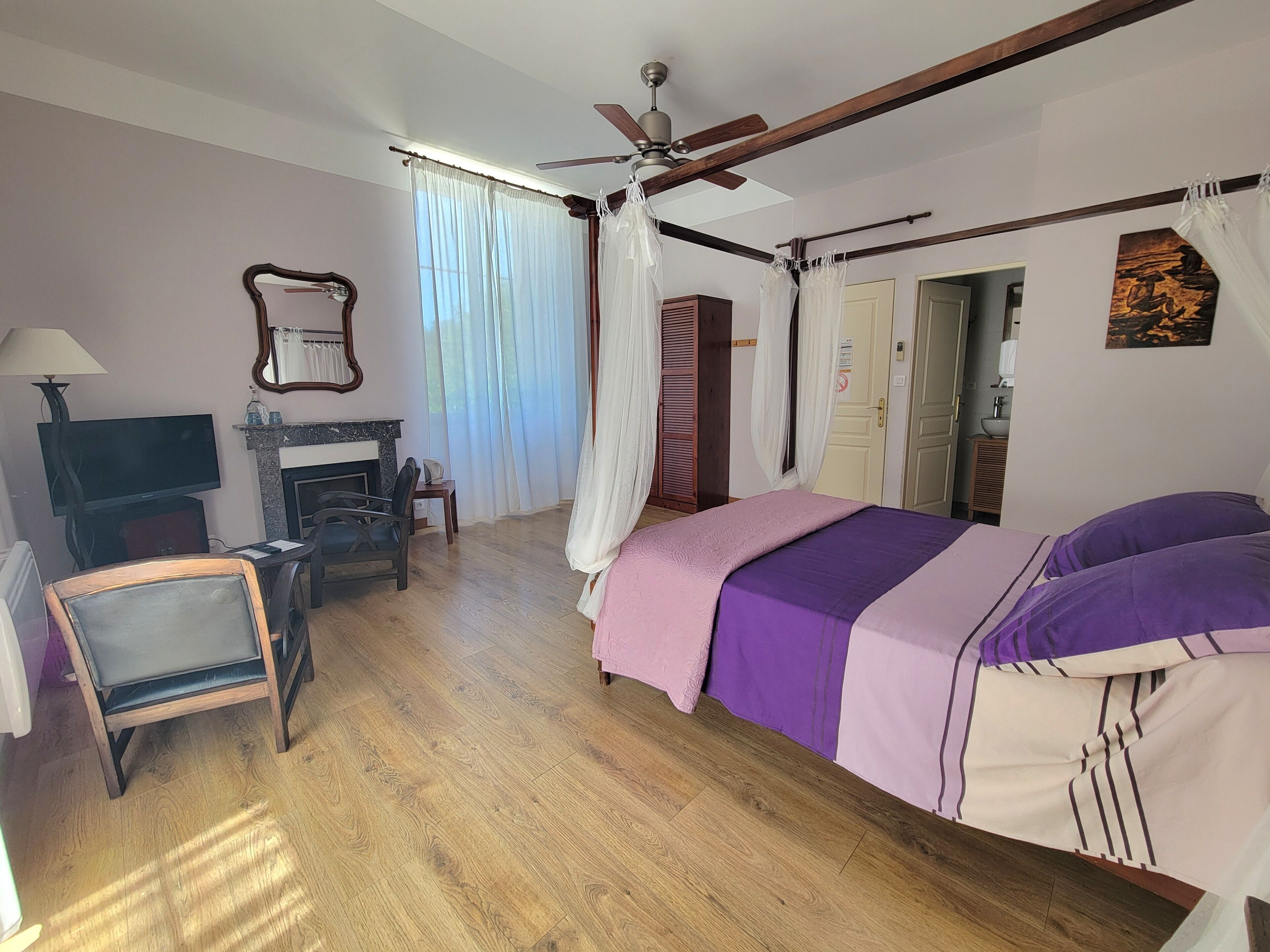 Un dormitorio con una cama, televisión, chimenea, ventilador de techo y una puerta.