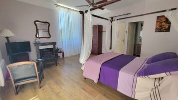 Un dormitorio con una cama, televisión, chimenea, ventilador de techo y una puerta.
