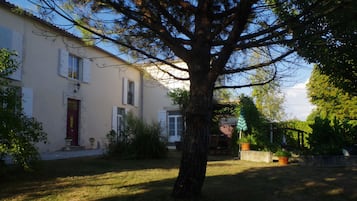 Ein Haus mit einem großen Baum im Vorgarten, weißer Fassade und roter Tür.
