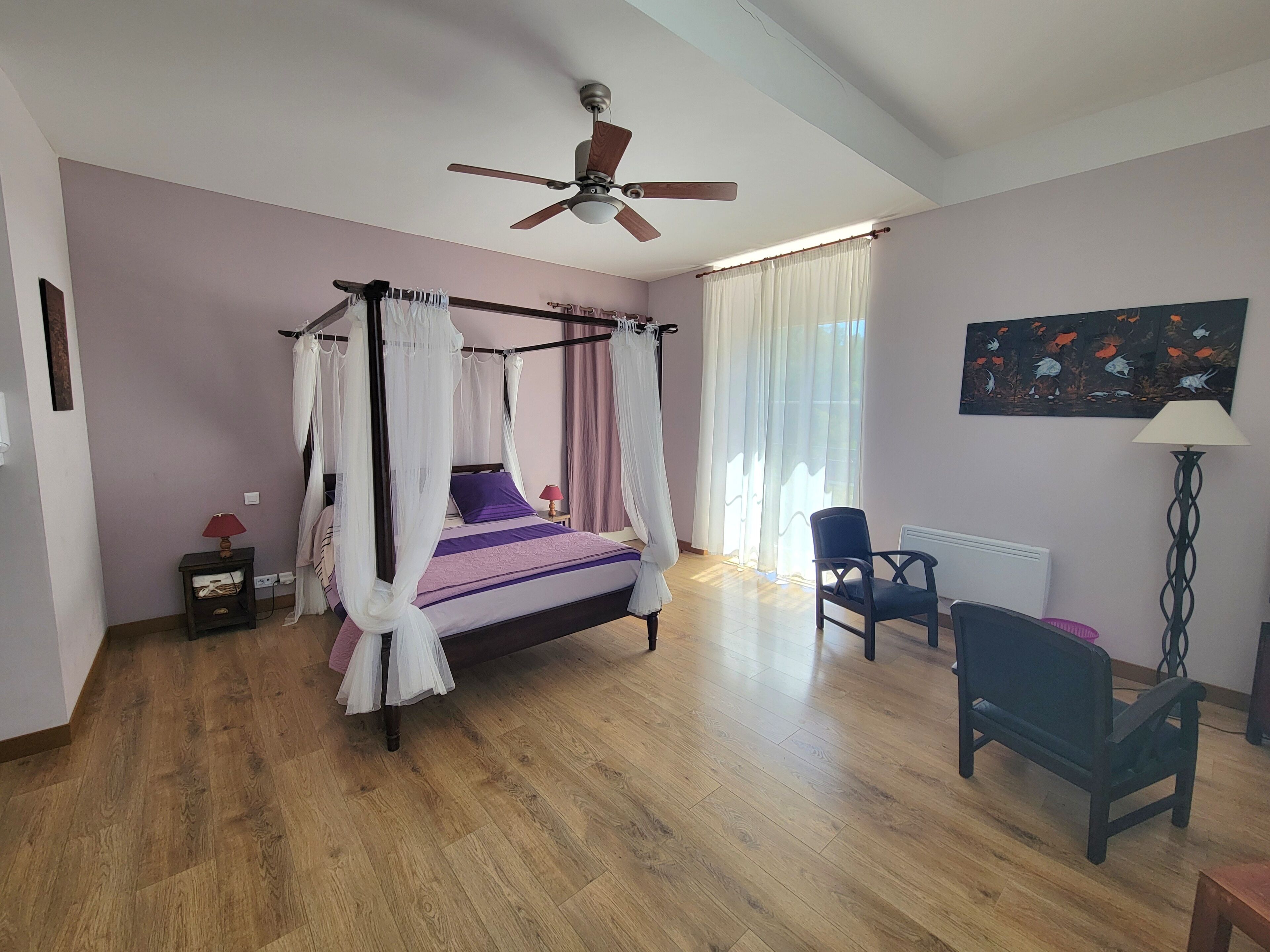 Une chambre à coucher avec un lit à baldaquin, un ventilateur de plafond, une chaise, un bureau et un tableau accroché au mur.