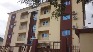 A multi-story building with a sign reading "Peacock House." It features balconies, air conditioning units, and a gated entrance. - Orchid Suite & Apartment (Abuja)