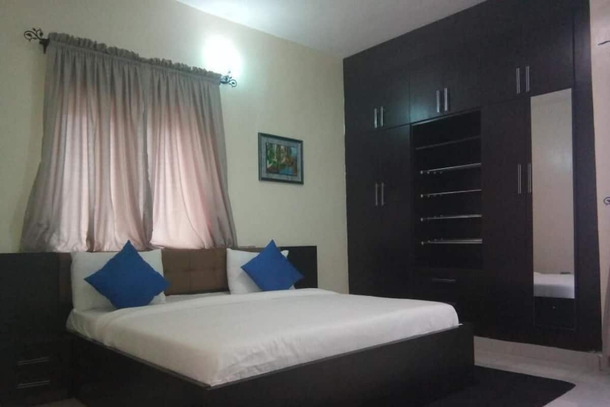 A bedroom with a bed, a wardrobe, a nightstand, and a window with curtains.