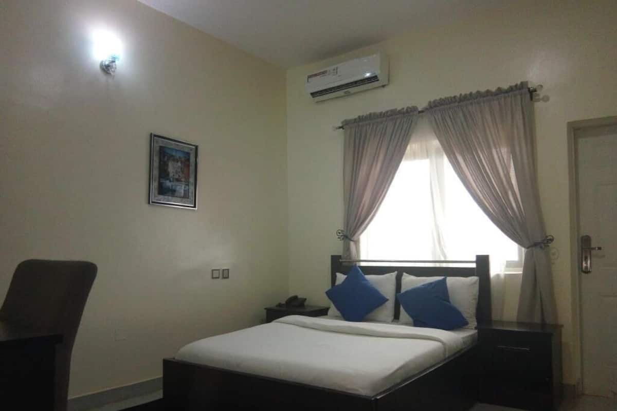 A bedroom with a bed, a chair, a nightstand, a wall-mounted air conditioner, and a door.