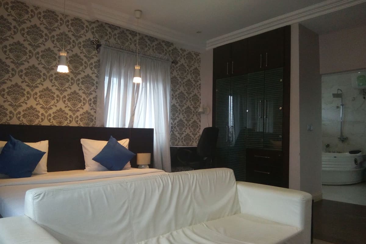 A hotel room with a bed, a white sofa, a desk, a chair, and a bathroom with a shower.