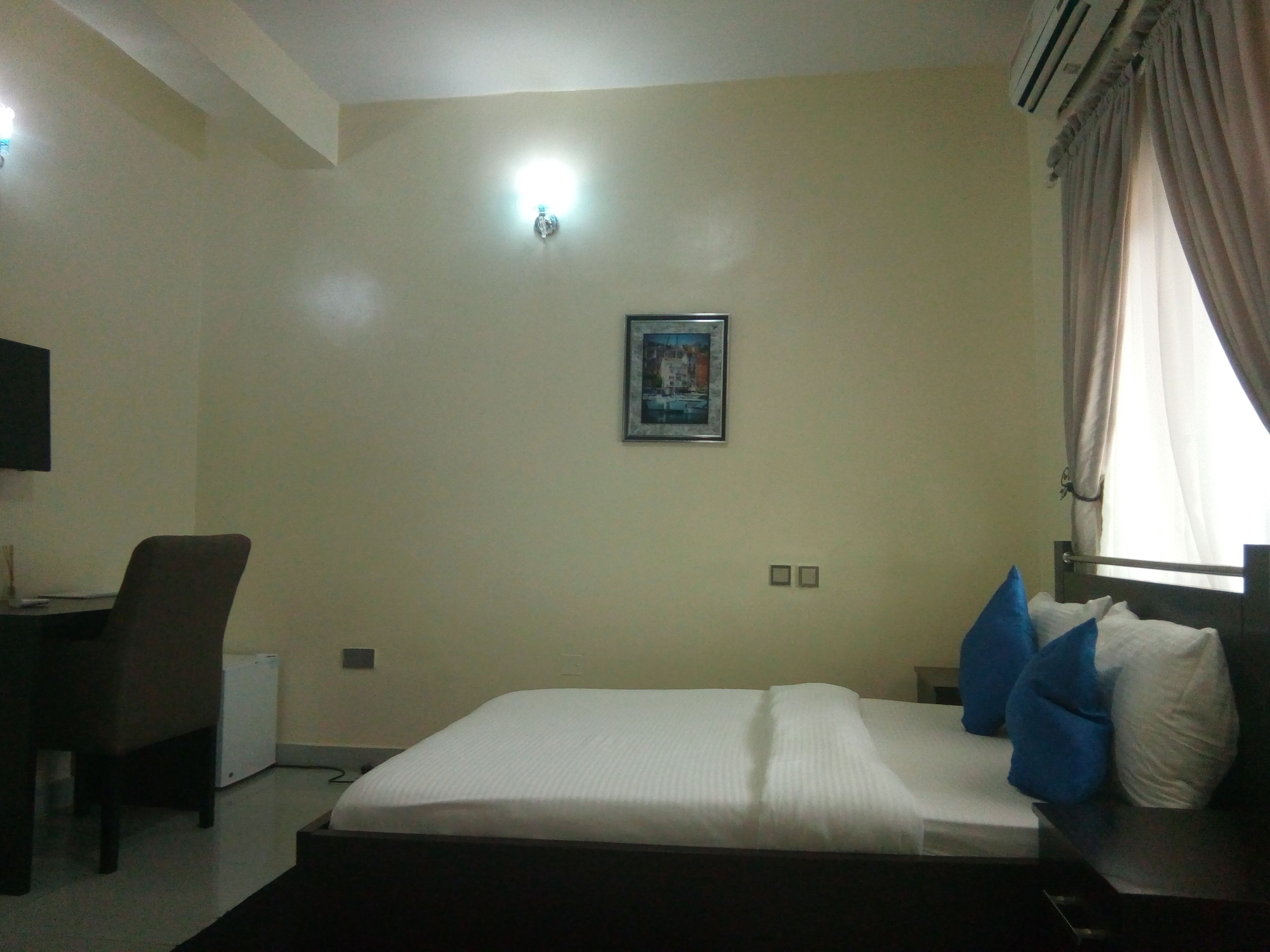 A hotel room with a bed, a desk, a chair, and a picture on the wall.