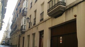 A narrow street with buildings on both sides, featuring balconies and a closed shop with a sign. - Apartamento El Patio de Cánovas (Cádiz)