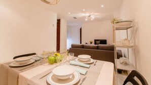 A dining area with a table set for four, a sofa in the background, and a shelf with kitchenware. - Apartamento El Patio de Cánovas (Cádiz)