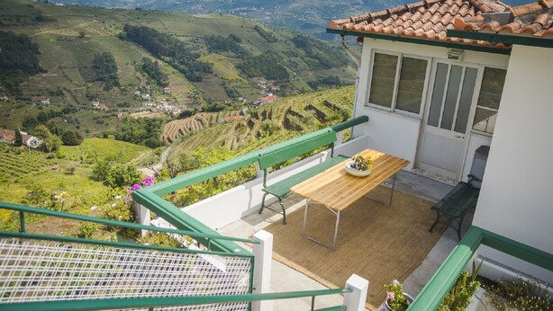 Un balcón con mesa y sillas de madera, con vistas a un viñedo y colinas lejanas.