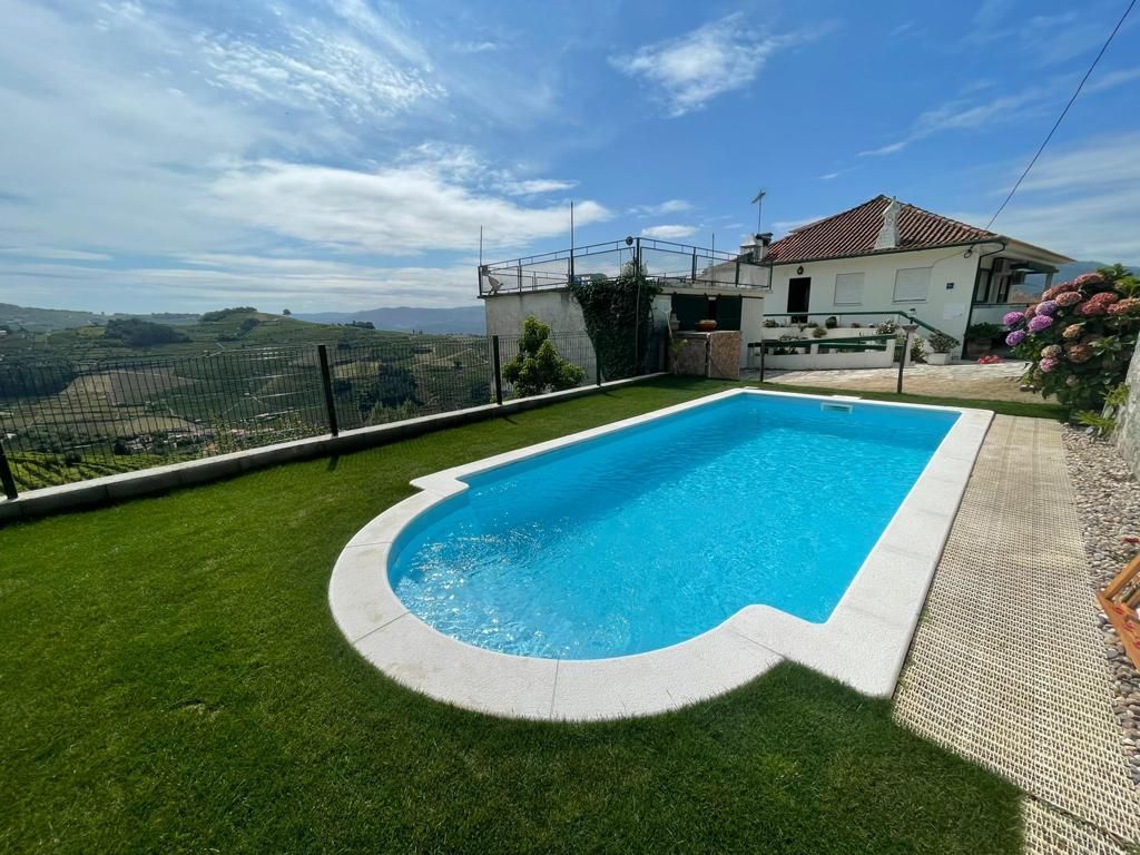 Une piscine entourée d’une pelouse, avec une maison en arrière-plan.