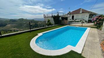 Une piscine entourée d’une pelouse, avec une maison en arrière-plan.