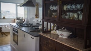 Una cocina con estufa a gas, horno y lavamanos. Hay un armario con puertas de vidrio que contiene diversos utensilios de cocina.