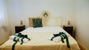 Una cama bien hecha con colcha color crema y dos lazos verdes atados a los almohadones.