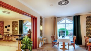 A dining area with a table and chairs, a potted plant, and a view of the outdoors through large windows. - Hotel Apfelblüte (Wendorf)