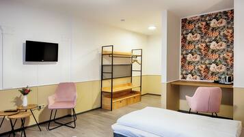 Ett hotellrum med en våningssäng, en tv som är monterad på väggen, en blommig tapet och två rosa stolar.
