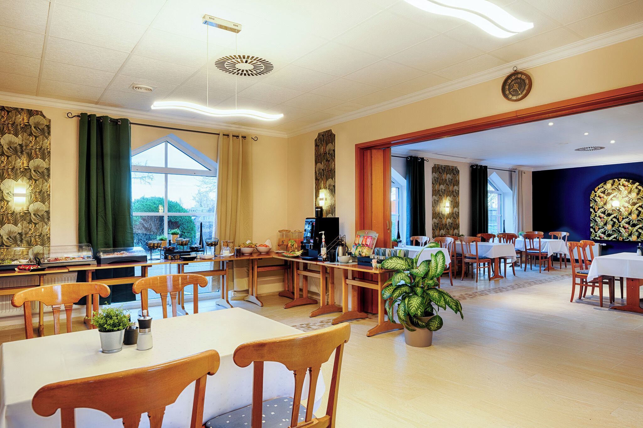 A spacious dining area with multiple tables and chairs, a large window with curtains, and a decorative wall with a clock.