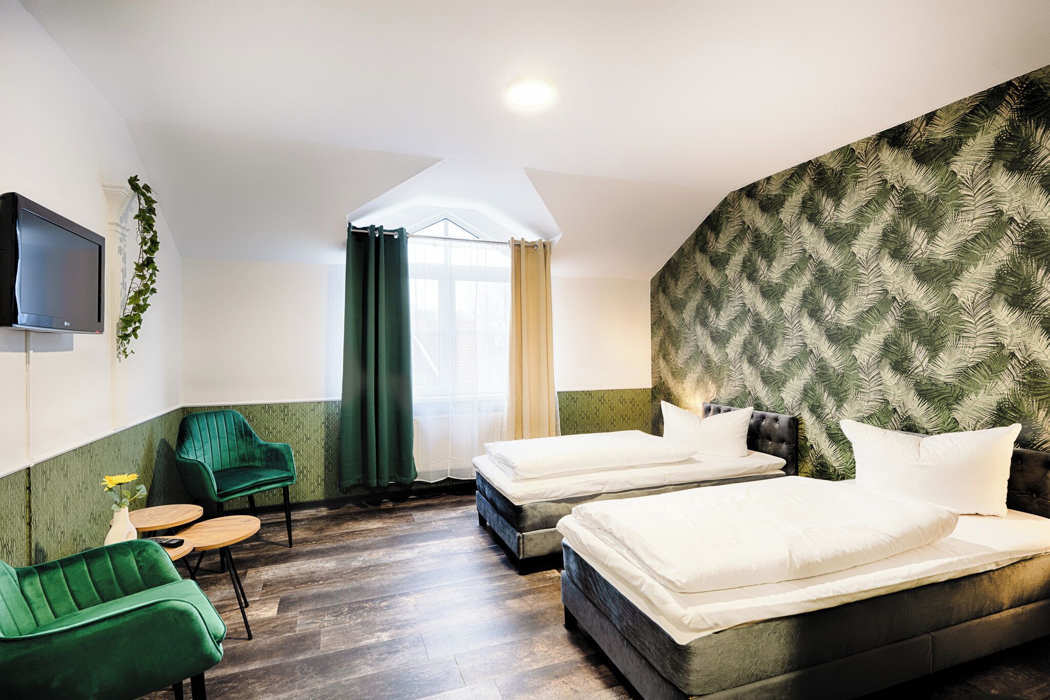 Een hotelkamer met twee bedden, een televisie, een klein tafeltje en een groene fauteuil.