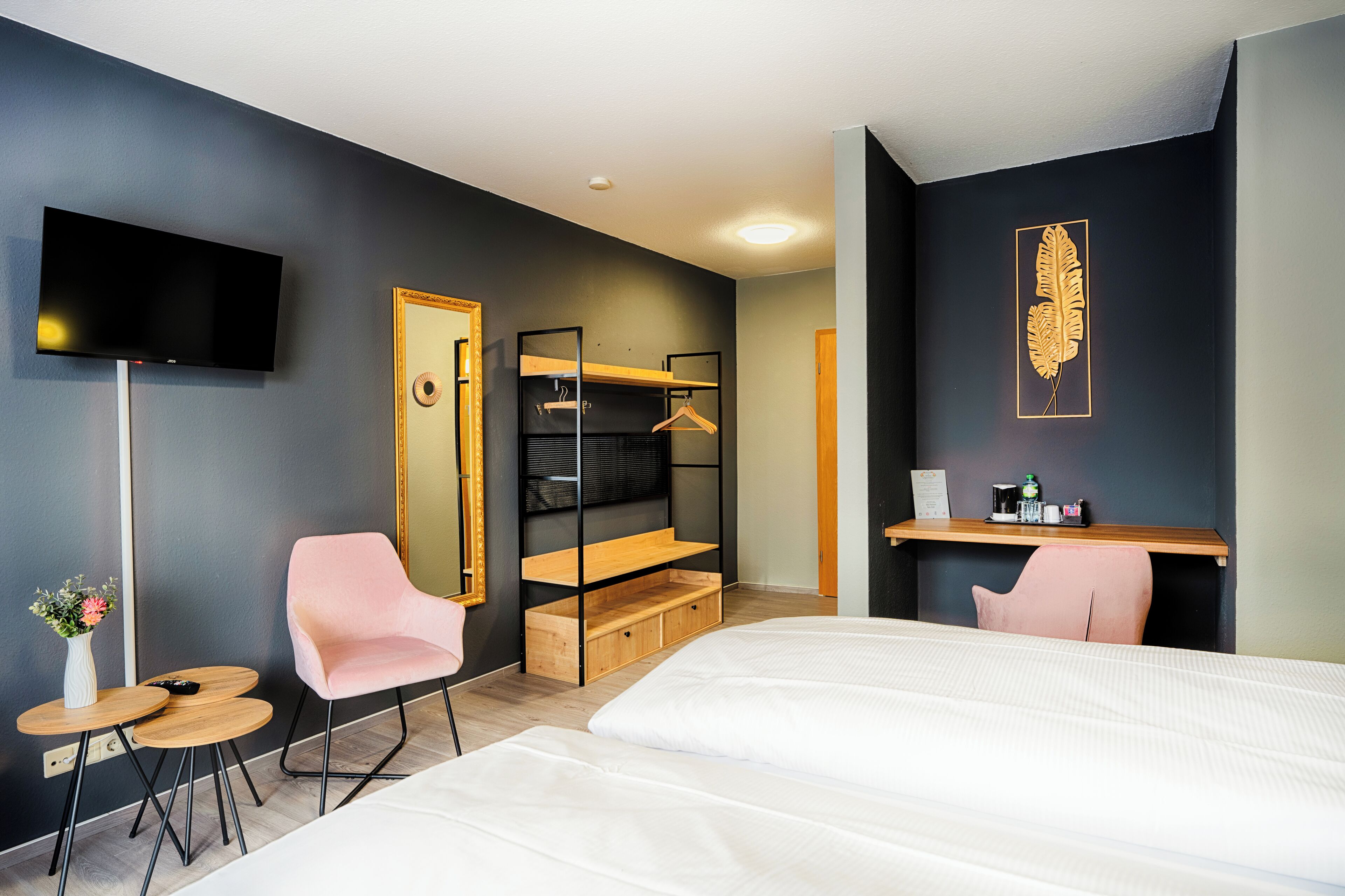 Ein modernes Hotelzimmer mit Bett, Fernseher, Spiegel, Holzregal, Schreibtisch und Stuhl.