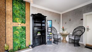 A lobby with a green vertical garden, a black bookshelf, two black wireframe chairs, a small round table with a plant, and a digital information kiosk. - Hotel Apfelblüte (Wendorf)