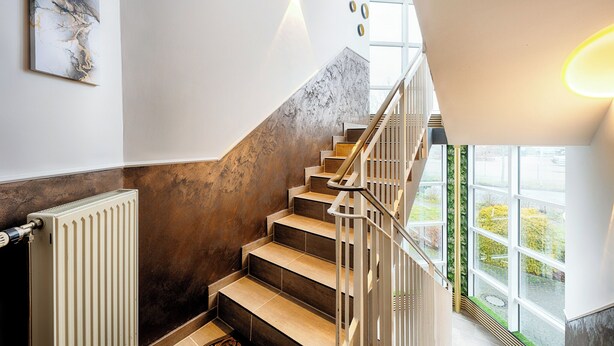 A modern staircase with a marble wall, a radiator, and a view of greenery outside. - Hotel Apfelblüte (Wendorf)