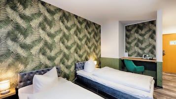 A hotel room with two beds, a green chair, a desk with a mirror, and a patterned wall.